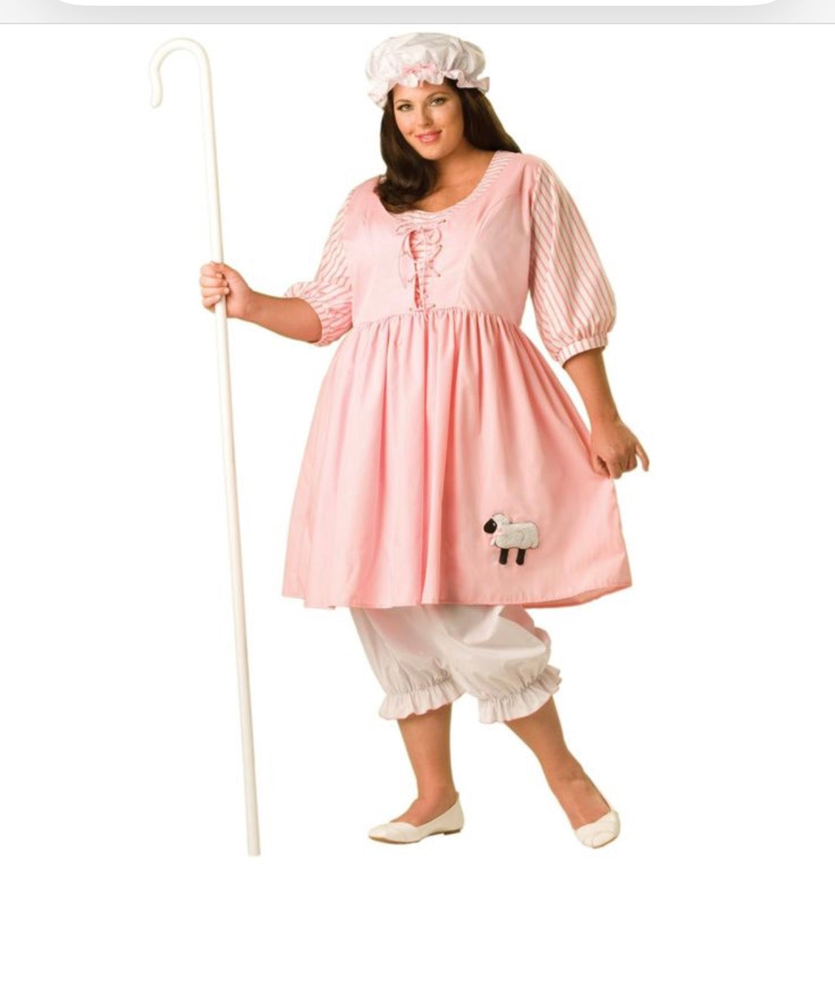 A woman modeling a pink and white Little bo Peep costume, featuring a pink dress with a sheep applique, white striped puff sleeves, white ruffled pants, a white bonnet, and holding a white shepherd's staff against a plain white background.