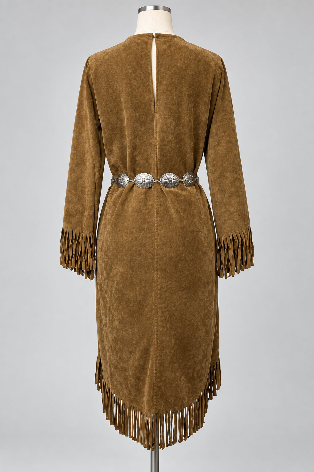 A brown suede fringe dress displayed on a mannequin from the back, featuring a silver concho belt at the waist and fringe detailing on the sleeves and hem.